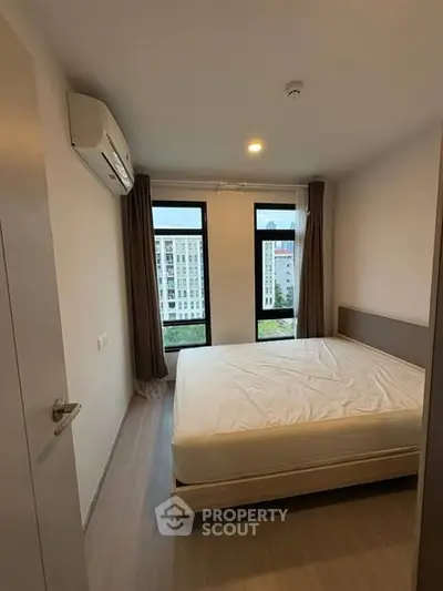 Modern bedroom with large windows and city view, featuring a comfortable bed and air conditioning.