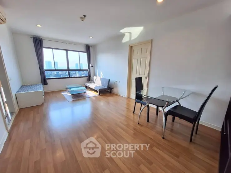 Spacious living room with wooden flooring and city view, featuring modern furniture and large windows.
