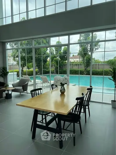 Luxurious living room with floor-to-ceiling windows overlooking a stunning pool and lush greenery.