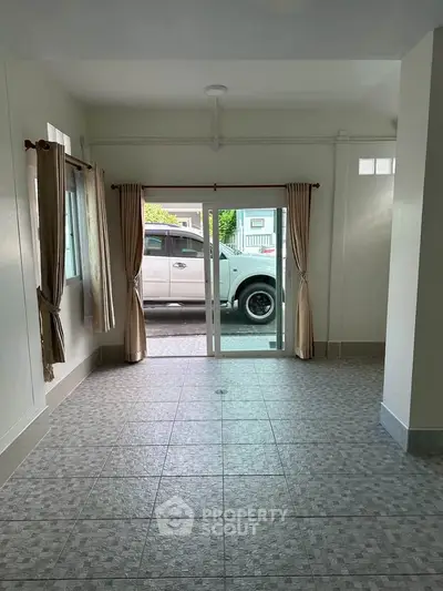 Spacious tiled room with sliding glass doors leading to a driveway, ideal for versatile living space.