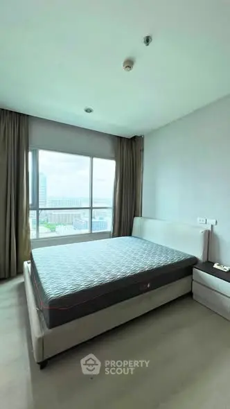 Spacious bedroom with large window offering city views, featuring a comfortable bed and modern decor.