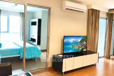Modern living room with TV and view into a stylish bedroom, featuring sleek furniture and large windows.