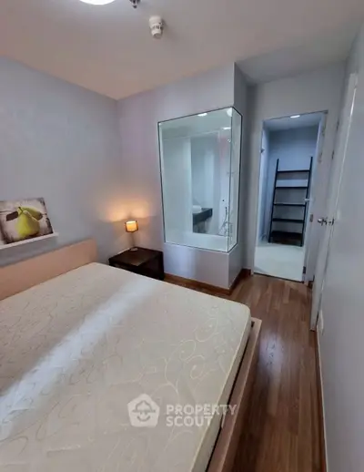 Cozy bedroom with wooden flooring and glass partition, featuring a modern design and ambient lighting.