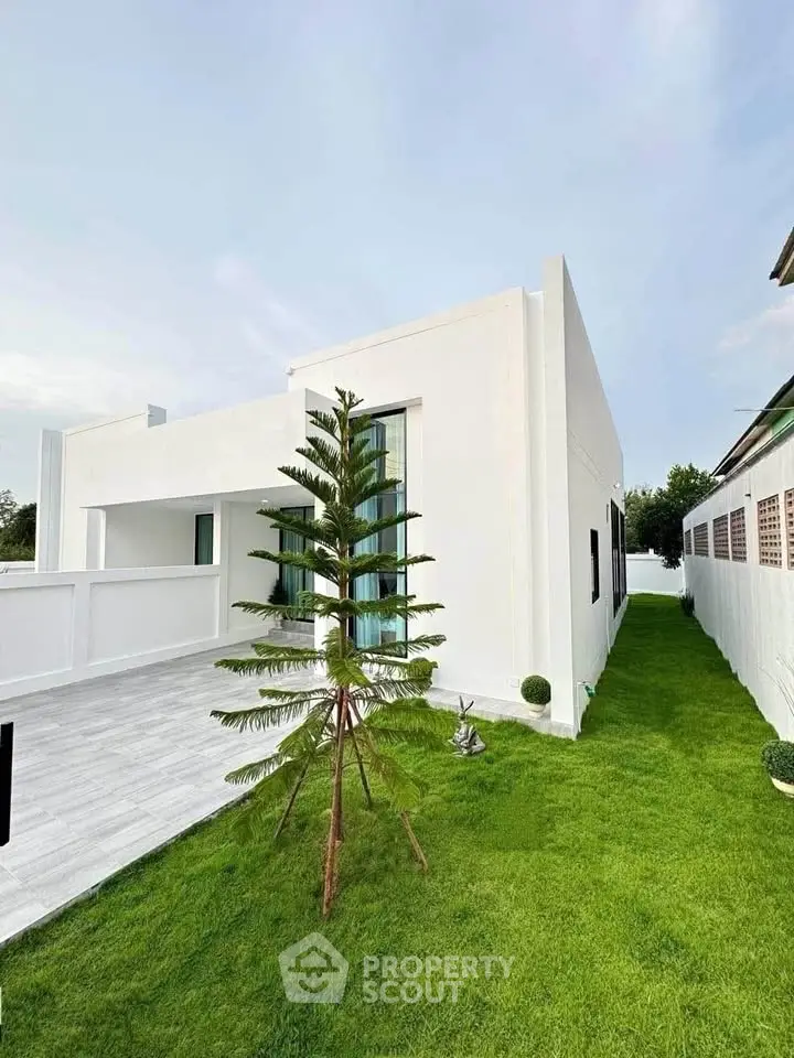 Modern white minimalist house with lush green lawn and sleek design.