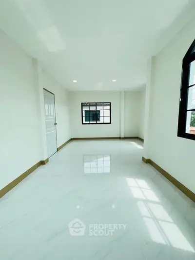 Spacious and bright room with large windows and glossy white flooring, perfect for modern living.