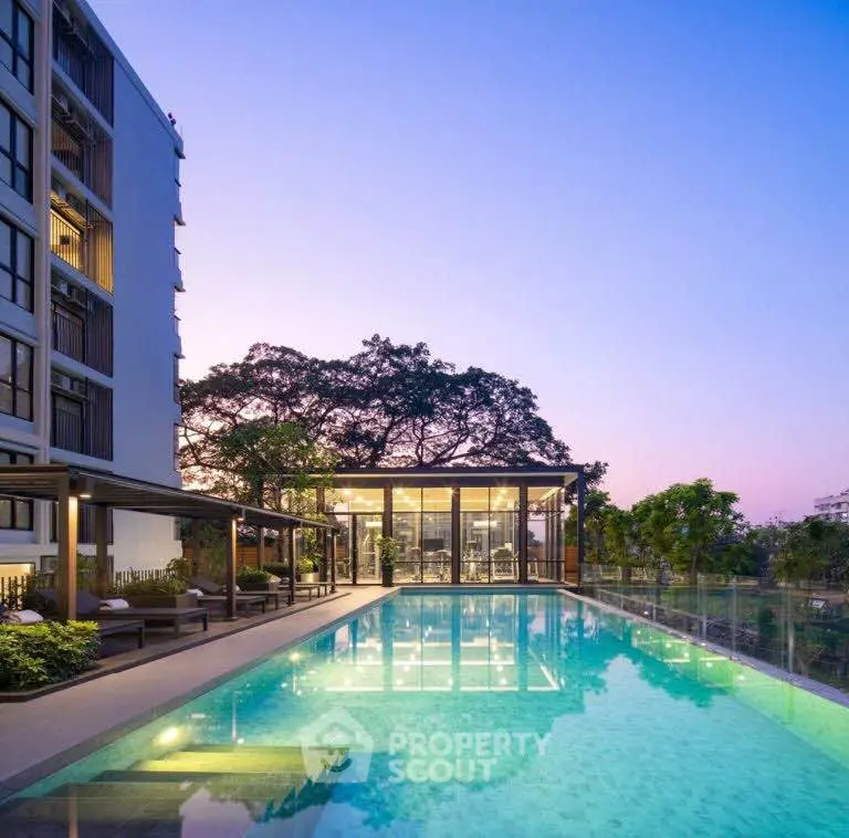 Luxurious apartment complex with stunning pool and modern glass building at sunset.