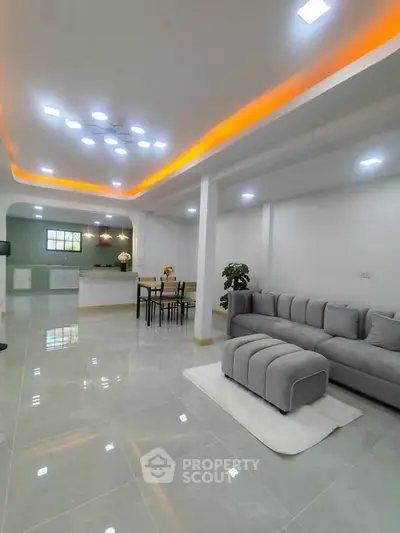 Spacious modern living room with open kitchen, elegant lighting, and sleek gray furniture.