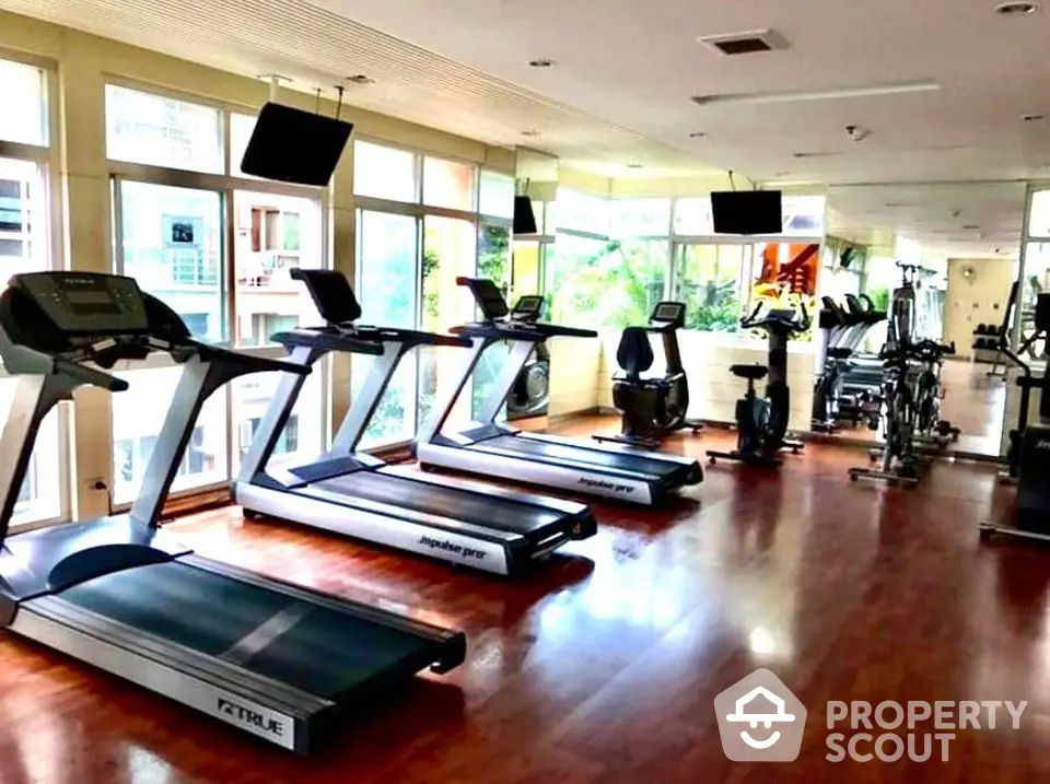 Spacious gym with modern equipment and large windows in luxury apartment complex.