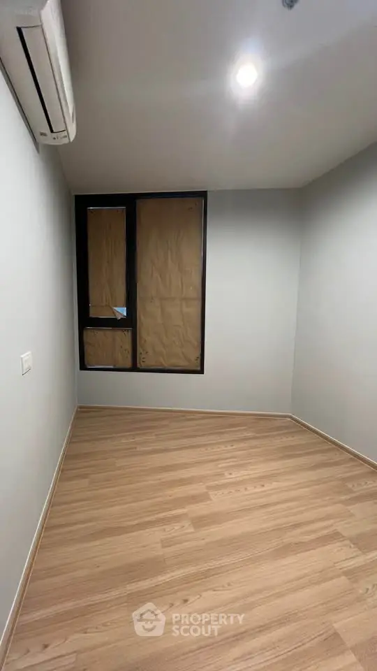 Minimalist empty room with wooden flooring and air conditioning, ready for customization.