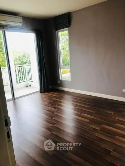 Spacious empty room with wooden flooring and balcony access, perfect for customization.