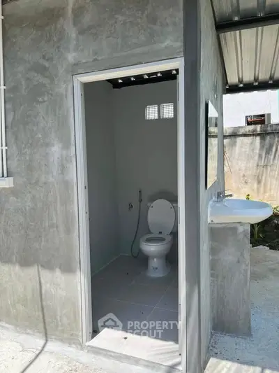Compact outdoor bathroom with modern concrete finish and open-air design.