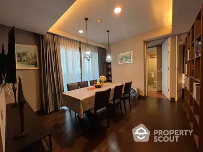 Elegant dining space with rich wooden flooring, modern chandelier, and a large table set for a family meal, adjacent to a cozy living area.