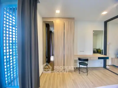 Modern bedroom with wooden wardrobe and sleek desk, featuring large windows for natural light.