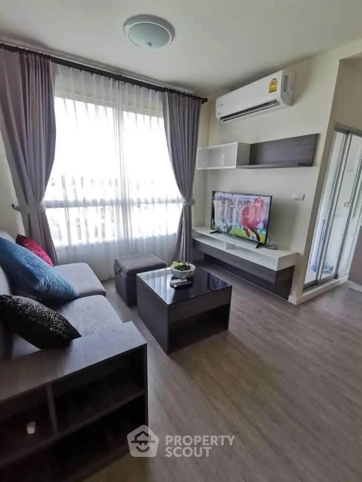 Modern living room with stylish furniture and natural light, featuring a sleek TV setup and air conditioning.
