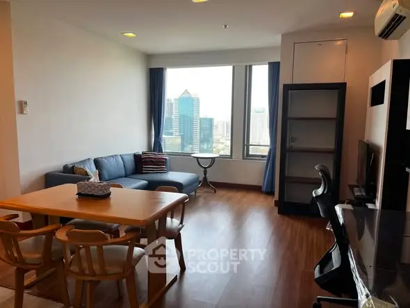 Spacious living room with city view, modern furniture, and wooden flooring in a high-rise apartment.