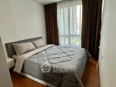 Modern bedroom with large window and city view, featuring a cozy double bed and elegant curtains.