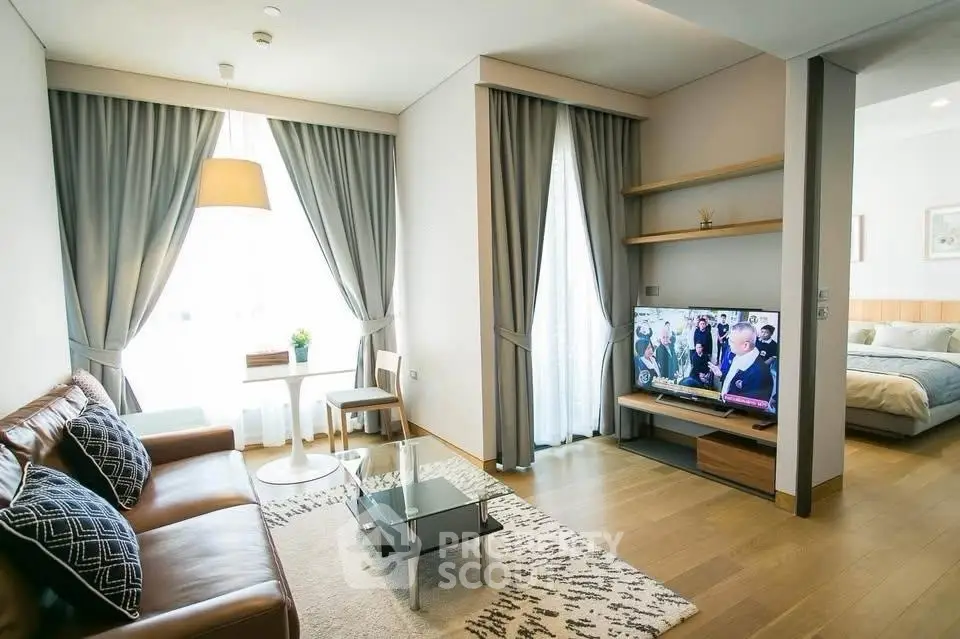 Modern living room with leather sofa and TV, adjacent to a cozy bedroom.