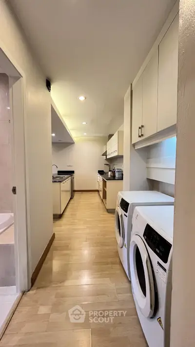 Spacious kitchen with modern appliances and laundry area, featuring sleek wooden flooring and ample storage.