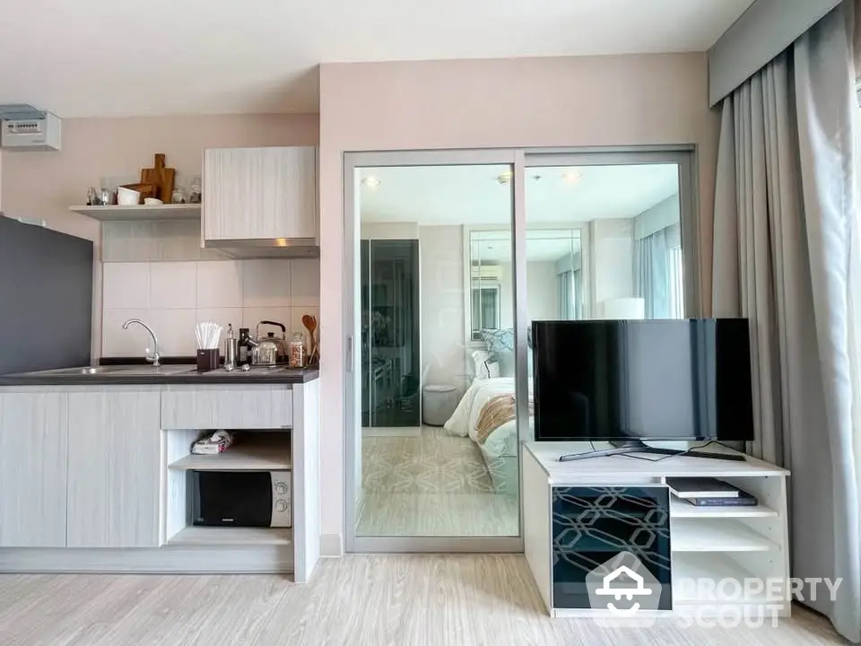 Modern studio apartment with sleek kitchen and cozy bedroom separated by glass partition.