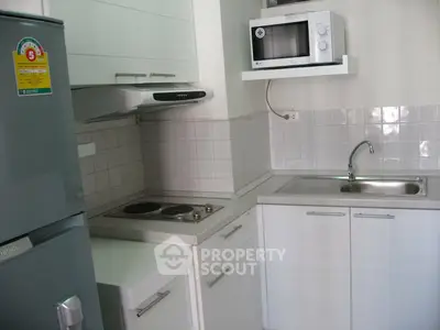 Compact modern kitchen with microwave, fridge, and electric stove in a sleek apartment.