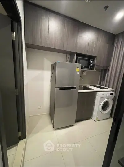 Modern kitchen with sleek cabinets, stainless steel fridge, microwave, and washing machine.