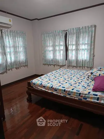 Cozy bedroom with wooden flooring and patterned curtains, featuring a comfortable bed.