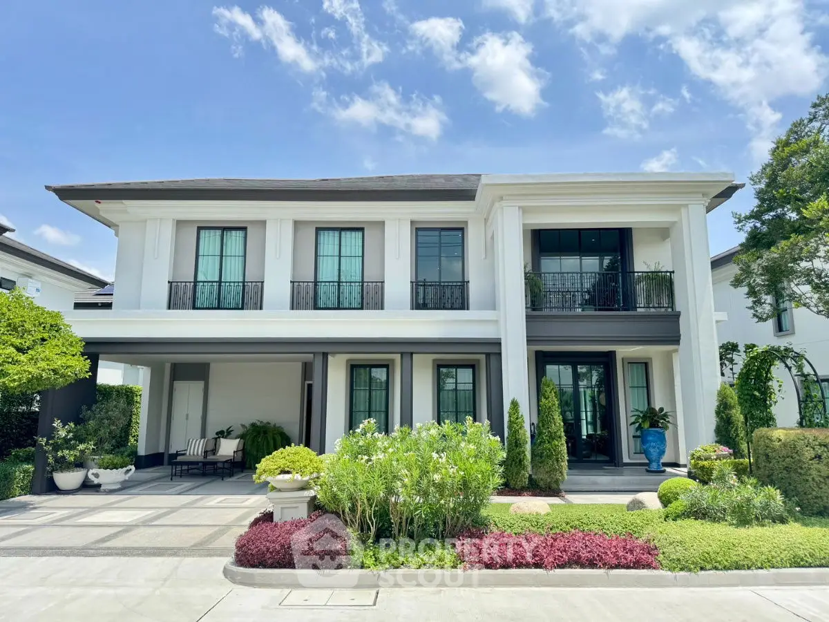Elegant two-story house with lush garden and modern facade under clear blue sky.