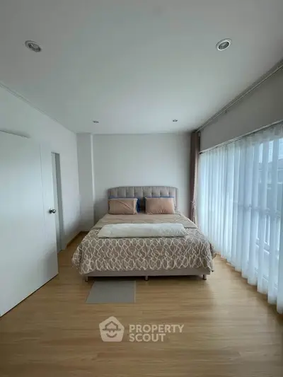 Spacious bedroom with large windows and elegant decor in modern apartment.
