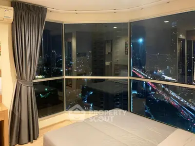 Luxurious bedroom with stunning city view through large corner windows at night.