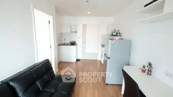 Modern studio apartment with sleek black sofa and compact kitchen area.