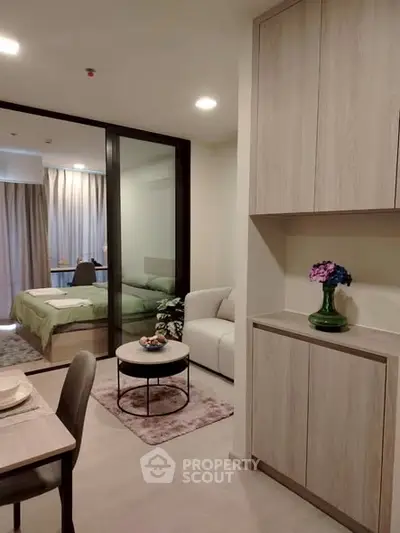 Modern studio apartment with open layout, featuring cozy living area and stylish bedroom separated by glass partition.