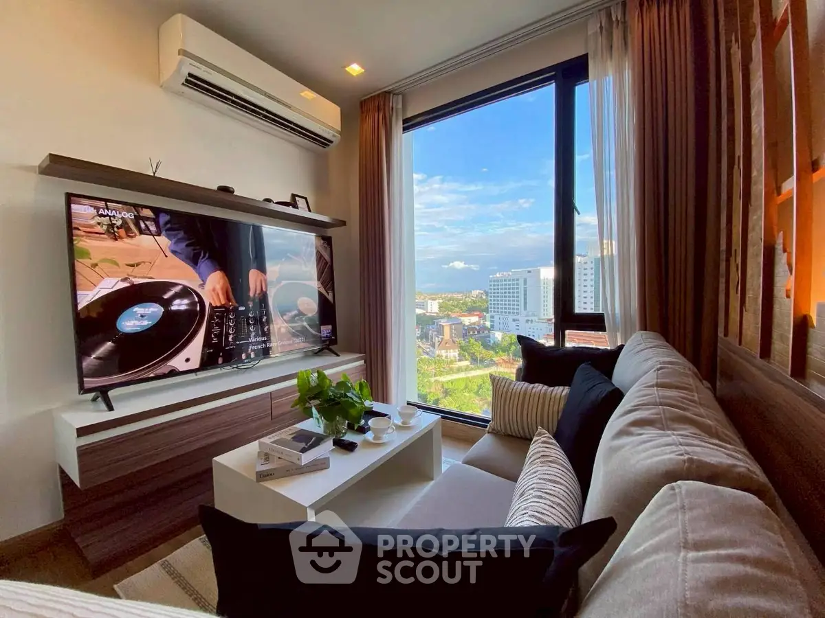 Modern living room with large window offering stunning city view, cozy sofa, and wall-mounted TV.