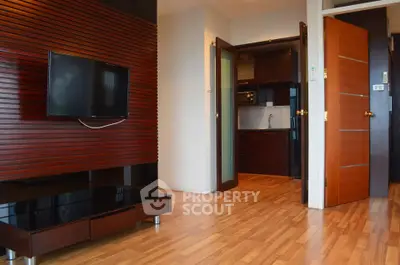 Modern living room with wooden flooring and sleek TV setup, leading to a compact kitchen.