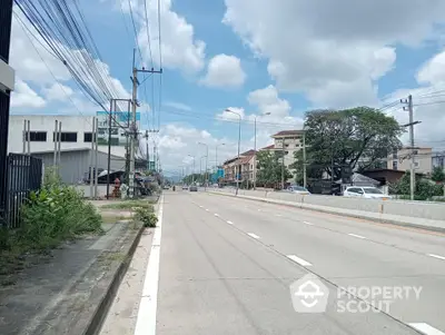 Spacious urban road with surrounding residential and commercial buildings under a clear blue sky.