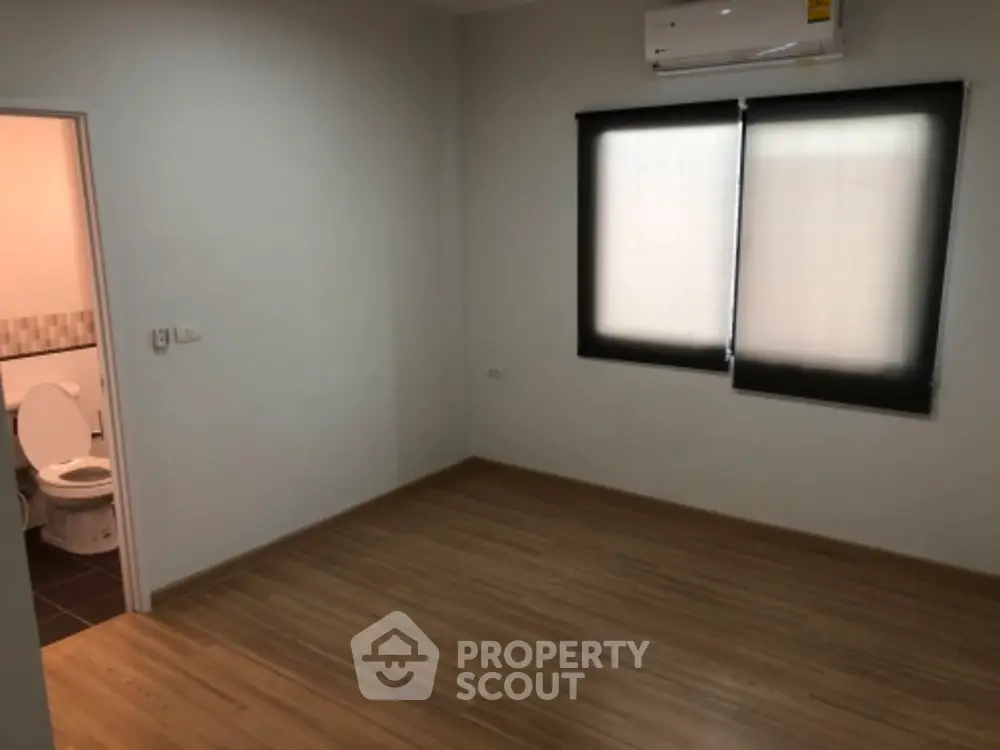 Spacious empty room with wooden flooring and adjacent bathroom.
