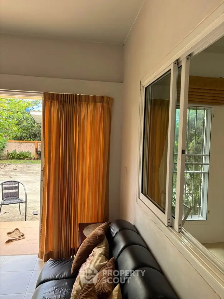 Cozy living room with sliding glass window and patio access, featuring a comfortable black leather sofa and warm curtains.