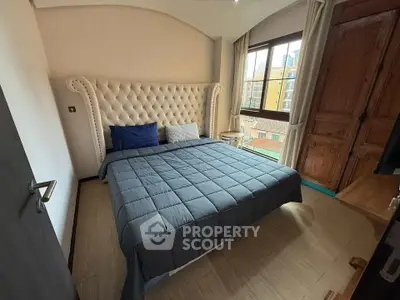 Cozy bedroom with elegant tufted headboard and large window offering city views.