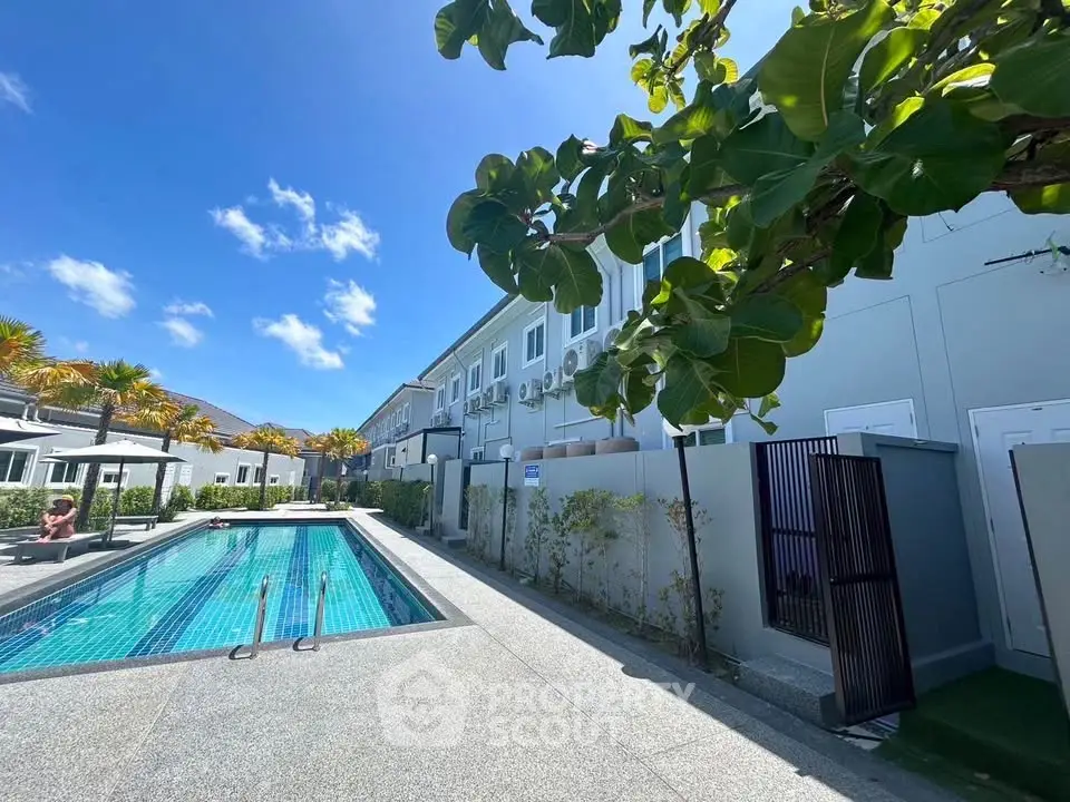 Modern residential complex with swimming pool and lush greenery under a clear blue sky.