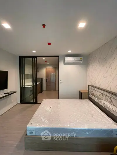 Modern bedroom with stylish decor and sliding glass doors leading to a kitchen area, featuring a mounted TV and air conditioning.
