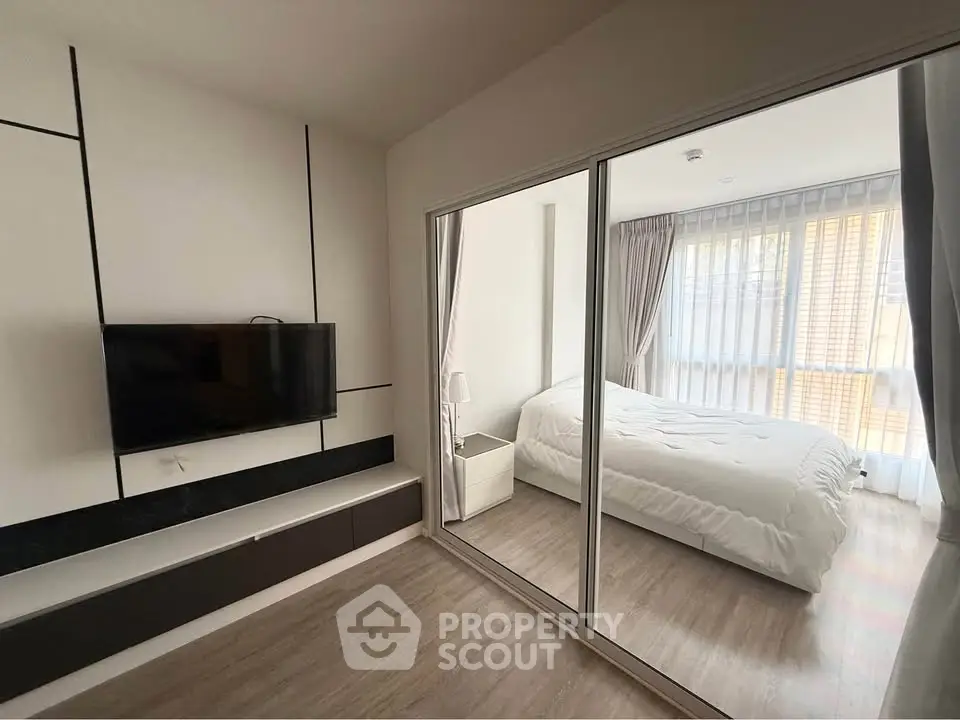 Modern bedroom with sleek design and natural light, featuring a wall-mounted TV and stylish decor.