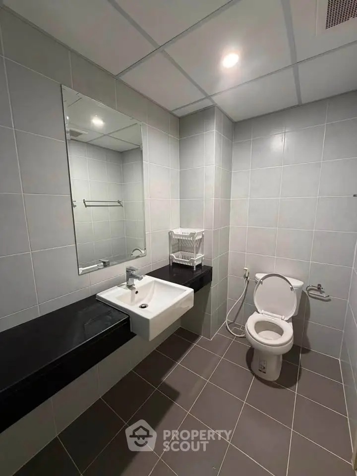 Modern bathroom with sleek tiles, wall-mounted sink, and toilet in a contemporary real estate property.