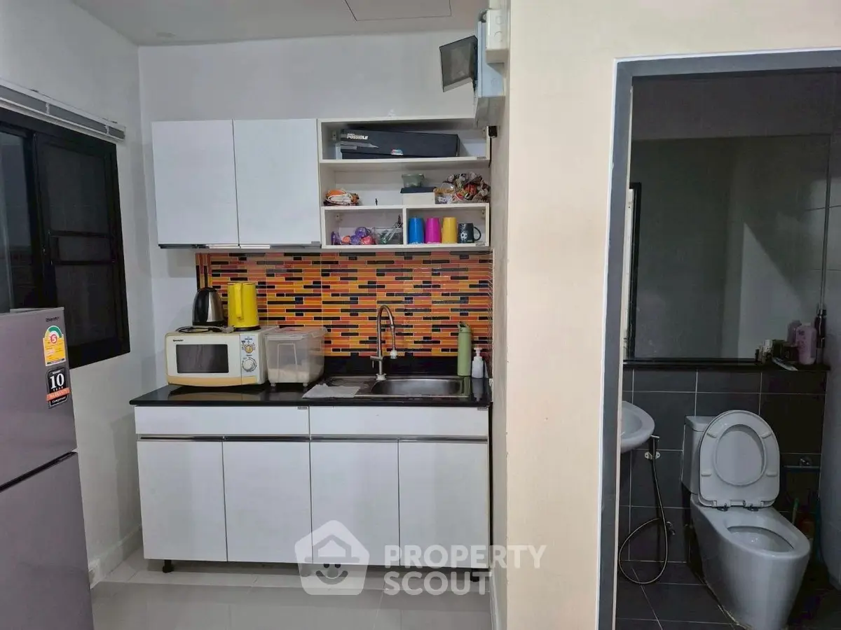 Modern compact kitchen with colorful backsplash and adjacent bathroom in urban apartment.