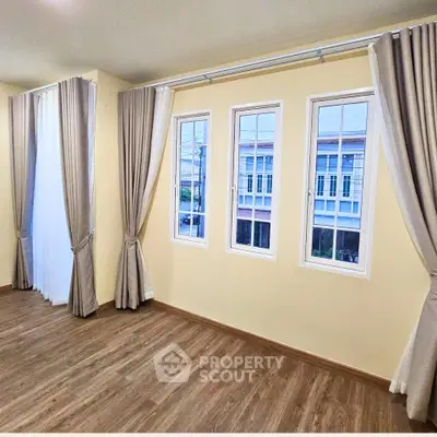 Spacious room with elegant curtains and large windows offering natural light and a view of neighboring buildings.