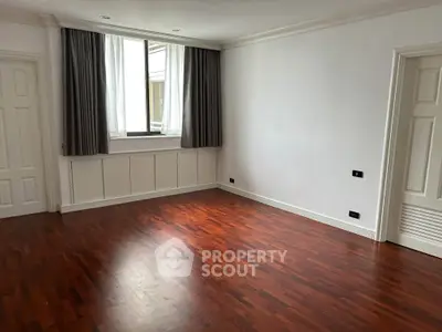 Spacious empty room with elegant wooden flooring and large window, perfect for customization.