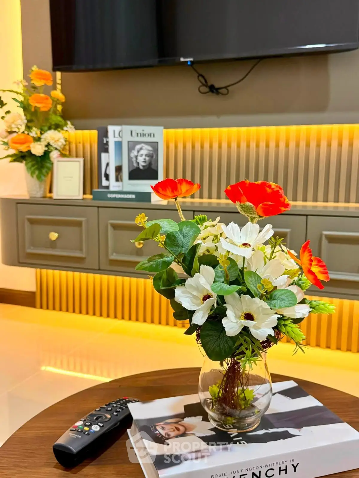 Stylish living room with modern decor, featuring a TV, elegant cabinetry, and vibrant floral arrangement.