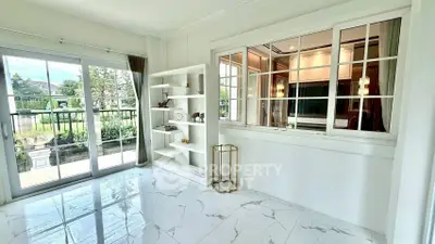 Bright room with large windows and garden view, featuring elegant white decor and modern shelving.
