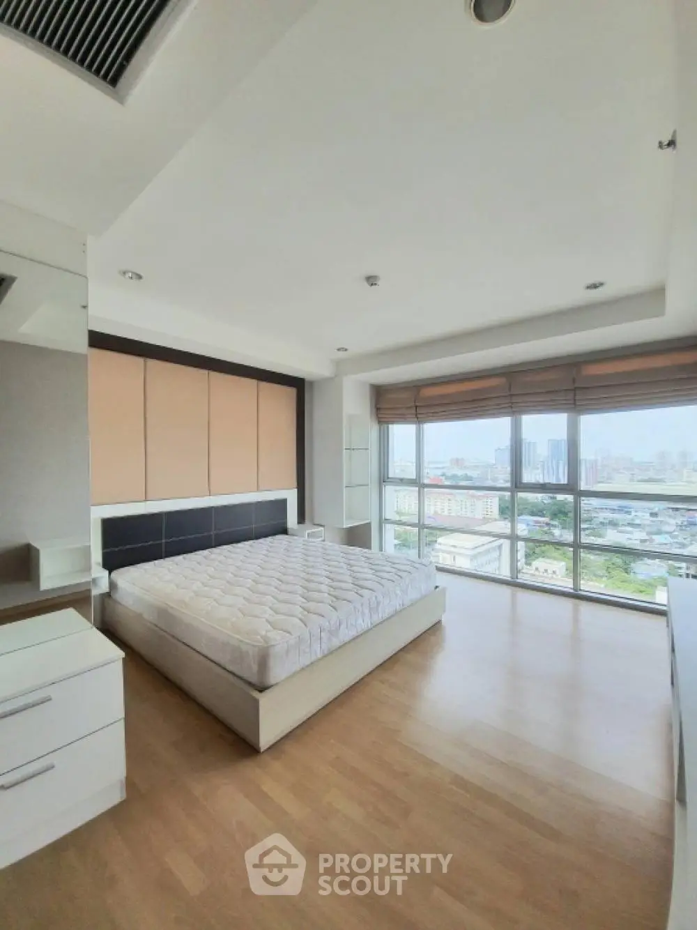Spacious bedroom with large windows offering stunning city views and natural light.