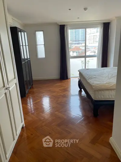 Spacious bedroom with elegant parquet flooring and large window offering city views.