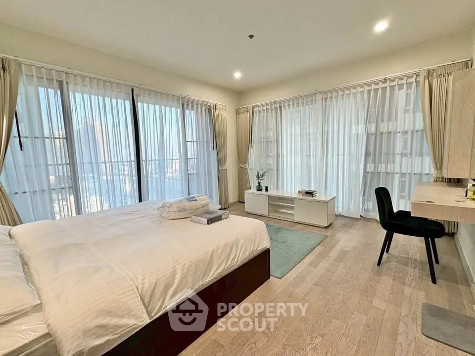 Spacious bedroom with large windows and modern furnishings in a luxury apartment.