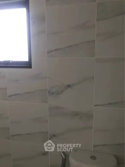 Modern bathroom with marble tiles and natural light from window.